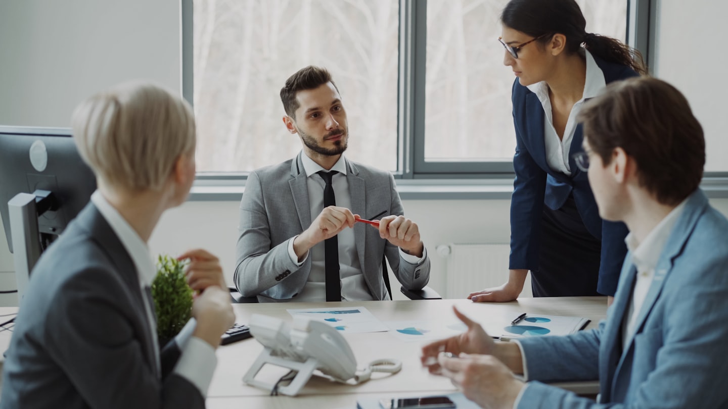 Business professionals discuss plans around a conference table.
